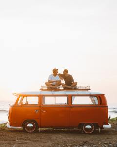 Two people sit atop a VW van on a beach