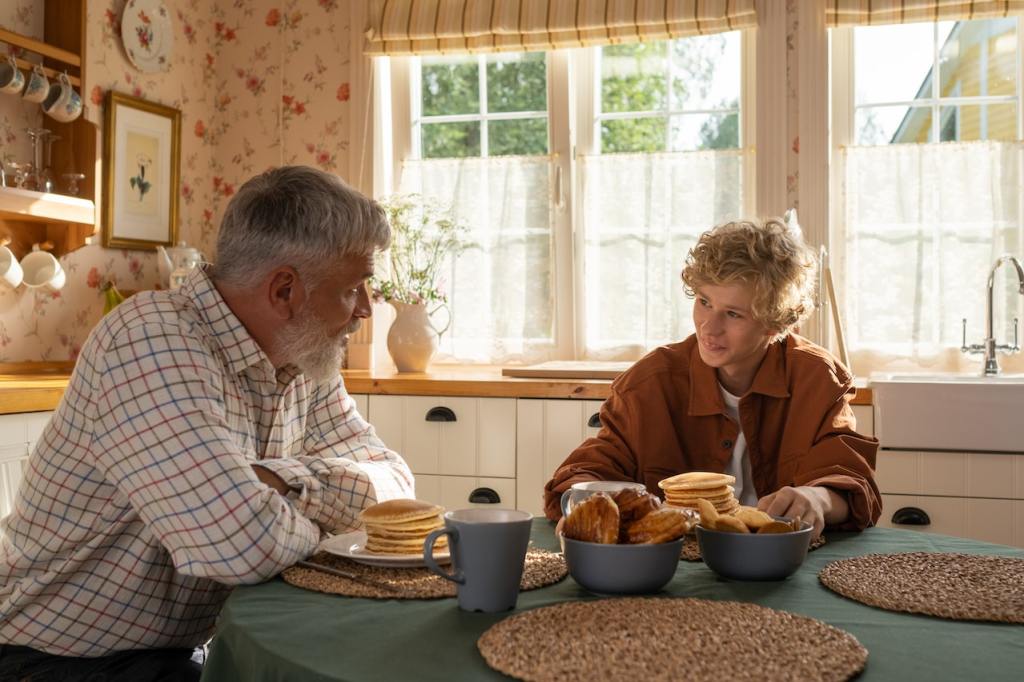 Teen boy and man sit at kitchen table with pancakes
